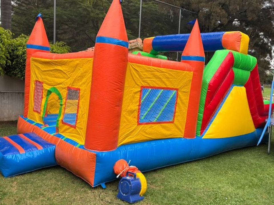 Combo inflable con torres naranjas y amarillas, brincolín central y resbaladilla lateral verde y amarilla